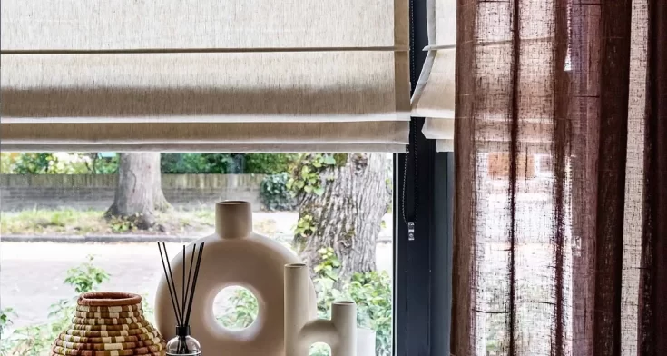 Beige vouwgordijn en transparante bruine gordijnen voor een sfeervol raam met decoratieve accessoires.