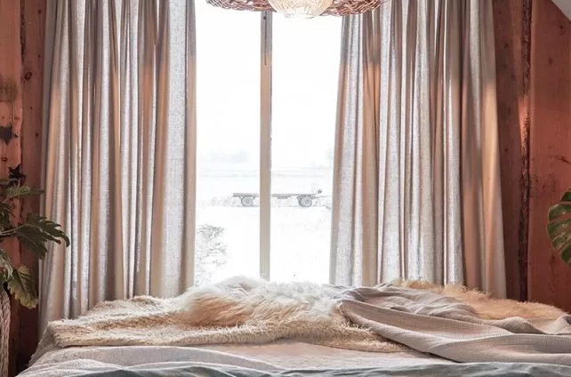 Knusse slaapkamer met een rustieke uitstraling, ingericht met linnen gordijnen, houten accenten en een zachte schapenvacht op het bed.