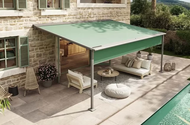 Stijlvolle pergola met groene doekzonwering creëert een schaduwrijke loungehoek bij een stenen huis met zwembad.