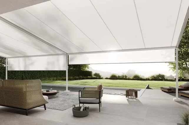 Moderne pergola met wit doek biedt schaduw op een stijlvolle terraslounge bij een zwembad met uitzicht op groen.