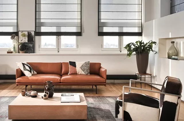 Moderne woonkamer met grote ramen voorzien van stijlvolle, transparante vouwgordijnen in grijstinten, die het natuurlijke licht filteren en een elegante uitstraling creëren.