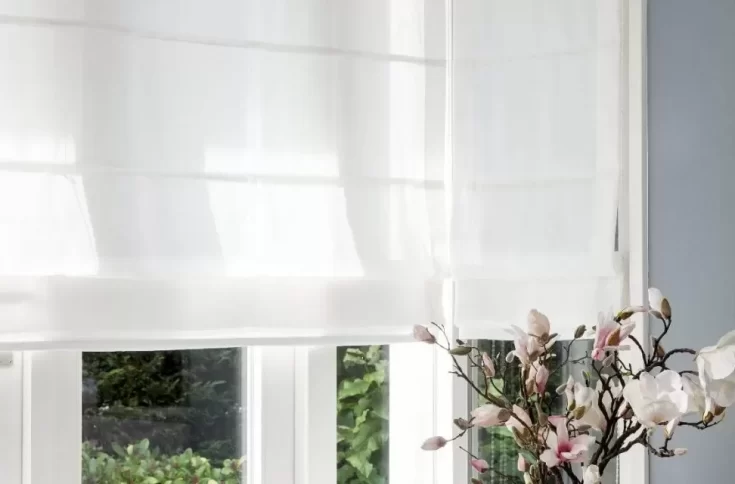 Witte vouwgordijnen filteren zacht het daglicht in een sfeervolle ruimte met een romantische touch, afgewerkt met bloeiende magnoliatak