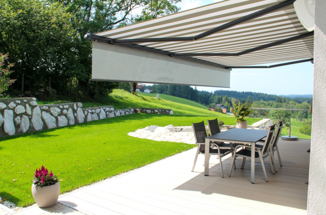 Terras met een uitschuifbaar zonnescherm, tuinset en uitzicht op een groen heuvellandschap
