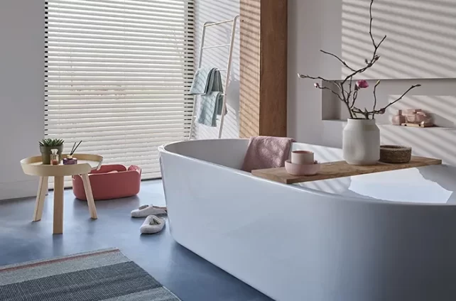 Badkamer met een rond wit bad en houten jaloezien voor de ramen