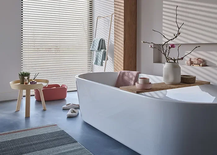 Badkamer met een rond wit bad en houten jaloezien voor de ramen