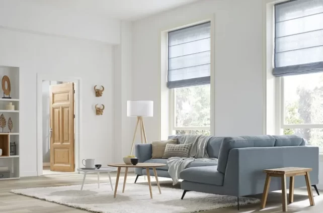 Ruime lichte woonkamer met grijze bank en lichtblauwe vouwgordijnen