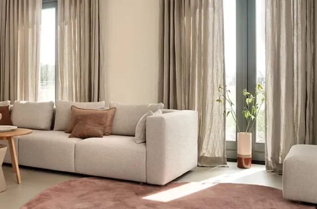 zacht gekleurde woonkamer in rozige neutrale tinten, met taupe gekleurde gordijnen die iets lichtdoorlatend zijn